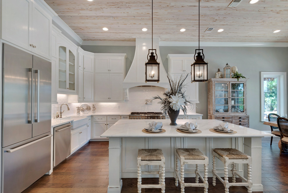 Inspiration for a large coastal l-shaped medium tone wood floor open concept kitchen remodel in Miami with a farmhouse sink, shaker cabinets, white cabinets, marble countertops, white backsplash, ceramic backsplash, stainless steel appliances and an island