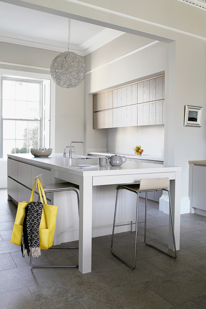 Example of a mid-sized trendy u-shaped limestone floor kitchen design in Dublin with flat-panel cabinets, stainless steel appliances, an island, an undermount sink, light wood cabinets, solid surface countertops, gray backsplash and marble backsplash