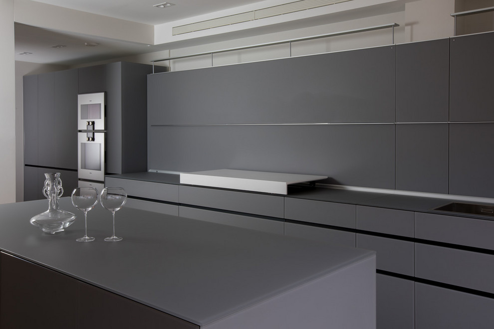 На фото: параллельная кухня среднего размера в стиле модернизм с обеденным столом, стеклянными фасадами, серыми фасадами, стеклянной столешницей, белым фартуком, фартуком из стекла, островом и серой столешницей