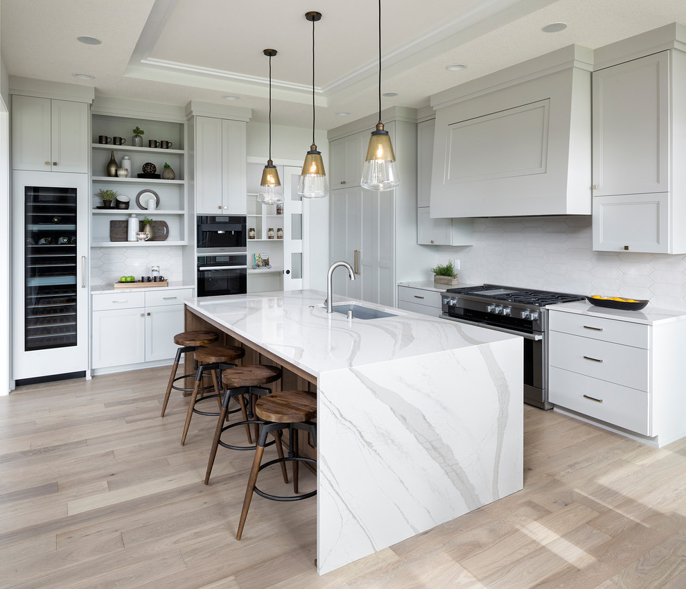 This is an example of a classic kitchen in Minneapolis with a submerged sink, recessed-panel cabinets, grey cabinets, white splashback, stainless steel appliances, light hardwood flooring, an island, beige floors and white worktops.