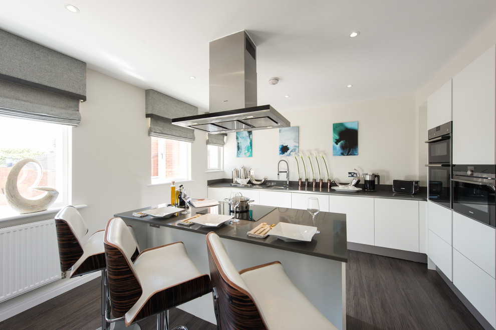Medium sized contemporary l-shaped kitchen in Buckinghamshire with flat-panel cabinets, white cabinets, an island and black worktops.