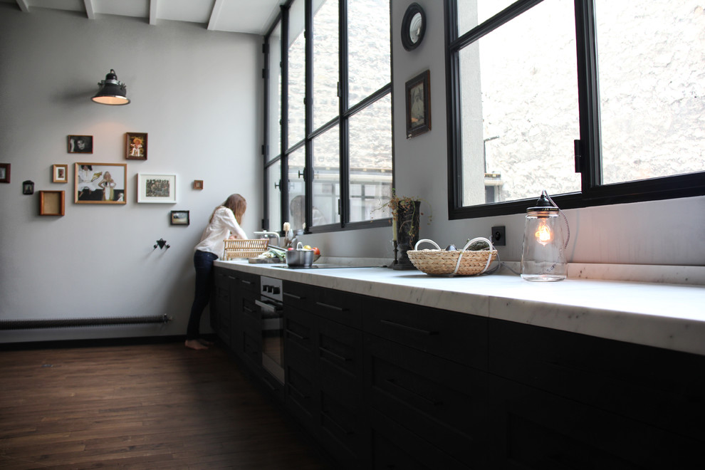 На фото: большая прямая кухня-гостиная в стиле ретро с мраморной столешницей, белым фартуком, техникой под мебельный фасад, темным паркетным полом и черно-белыми фасадами с