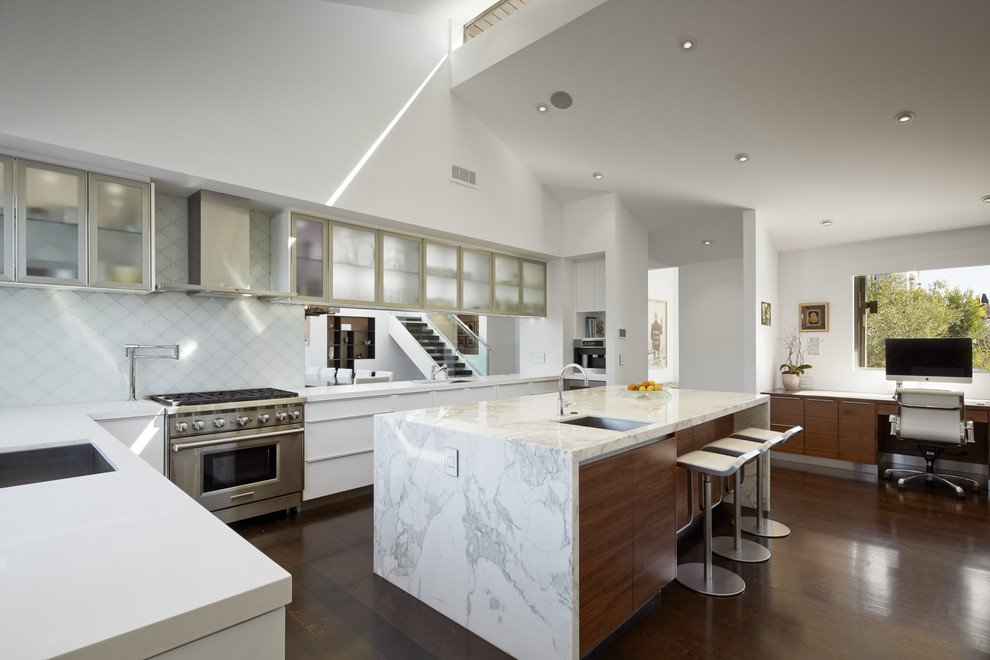 Moderne Küche mit Unterbauwaschbecken, Glasfronten, Küchengeräten aus Edelstahl, braunem Holzboden, Kücheninsel und Küchenrückwand in Weiß in Los Angeles