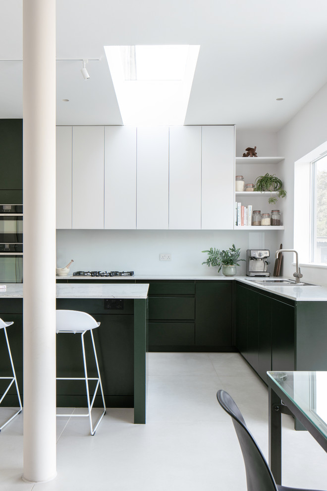 Mid-sized minimalist l-shaped ceramic tile and white floor open concept kitchen photo in London with a double-bowl sink, flat-panel cabinets, green cabinets, quartz countertops, black appliances, an island and white countertops