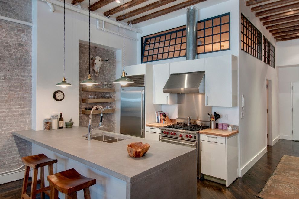 Zweizeilige Industrial Küche mit Betonarbeitsplatte, Küchengeräten aus Edelstahl, Doppelwaschbecken, flächenbündigen Schrankfronten und weißen Schränken in New York