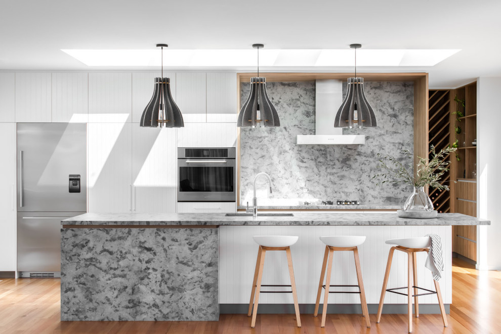 Idéer för att renovera ett funkis grå grått kök, med vita skåp, granitbänkskiva, rostfria vitvaror, släta luckor, grått stänkskydd, mellanmörkt trägolv, en köksö och brunt golv