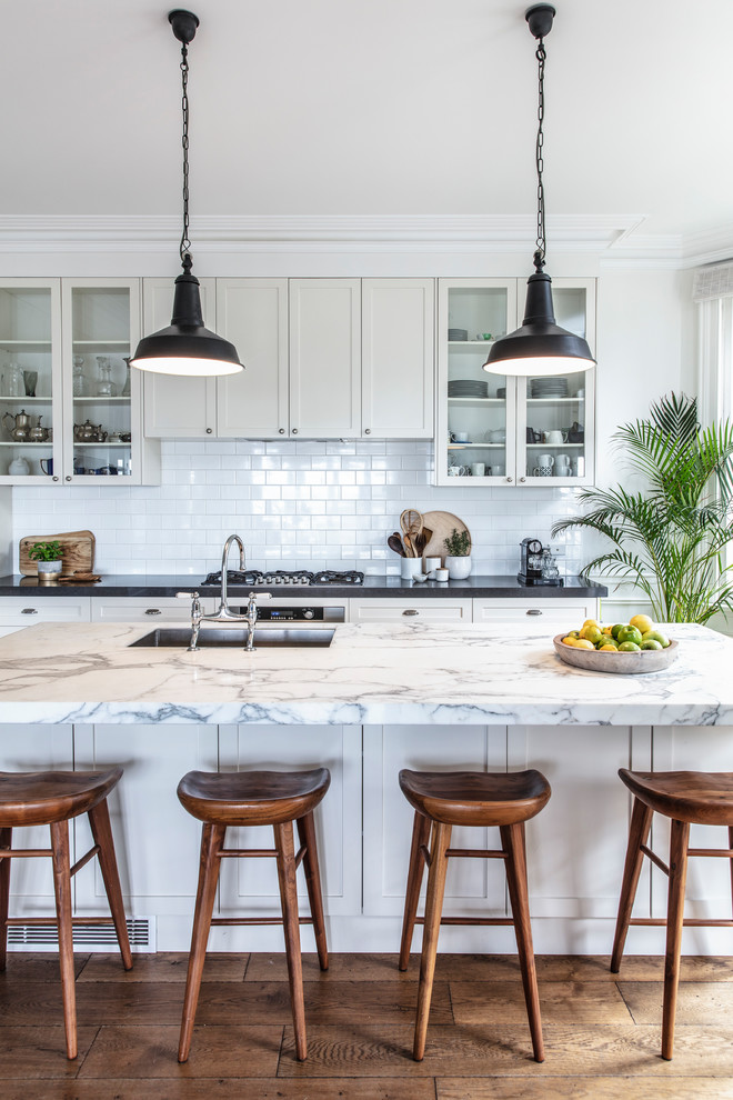 Inspiration for a large contemporary l-shaped medium tone wood floor eat-in kitchen remodel in Other with a single-bowl sink, shaker cabinets, white cabinets, marble countertops, white backsplash, subway tile backsplash, stainless steel appliances, an island and white countertops