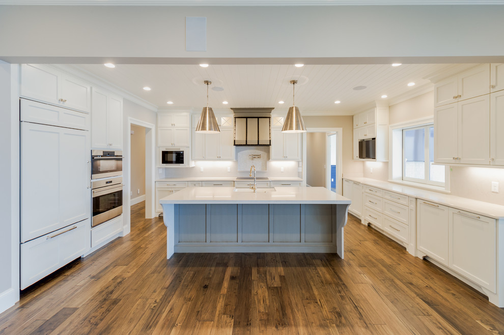 Foto på ett stort lantligt vit linjärt kök och matrum, med en undermonterad diskho, luckor med infälld panel, vita skåp, bänkskiva i kvarts, integrerade vitvaror, mellanmörkt trägolv, en köksö och brunt golv