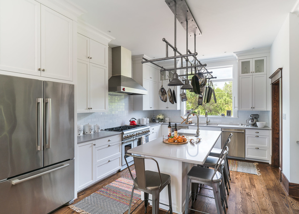 Example of a mid-sized ornate brown floor and medium tone wood floor kitchen design in Austin with recessed-panel cabinets, white cabinets, subway tile backsplash, stainless steel appliances, an island, a double-bowl sink, quartz countertops, white backsplash and gray countertops