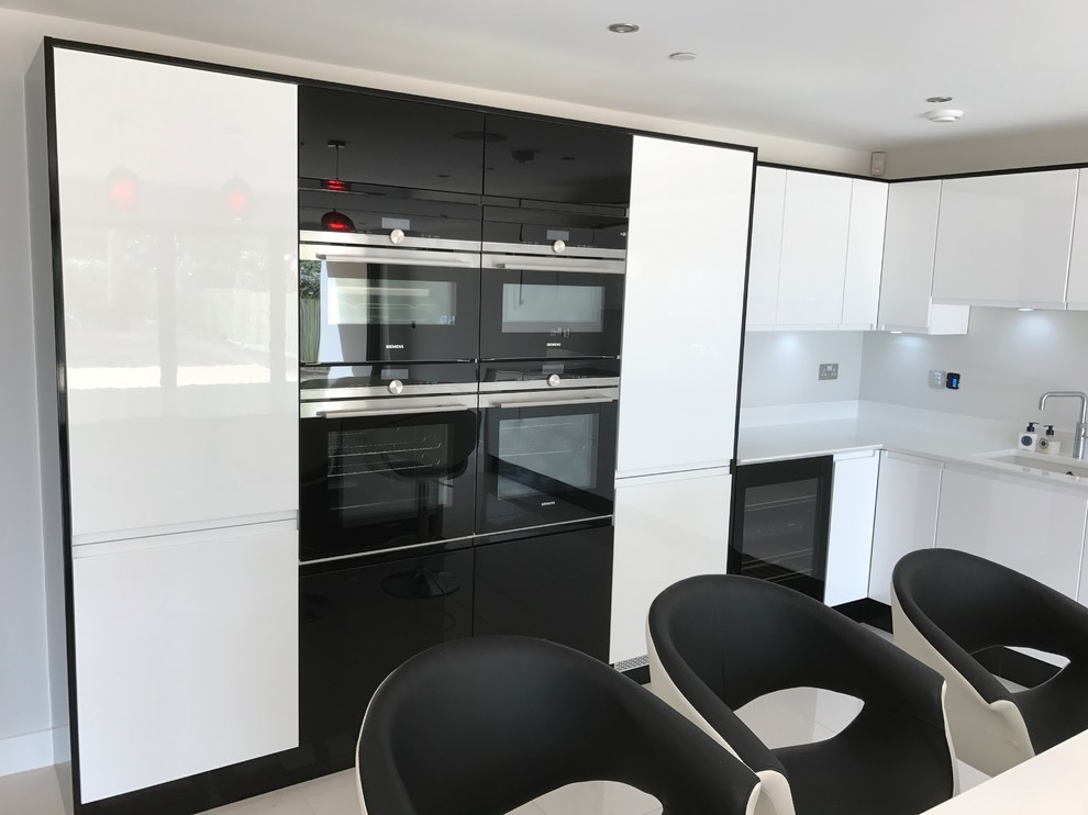 Photo of a large contemporary l-shaped open plan kitchen in Dorset with a built-in sink, flat-panel cabinets, white cabinets, quartz worktops, integrated appliances and an island.