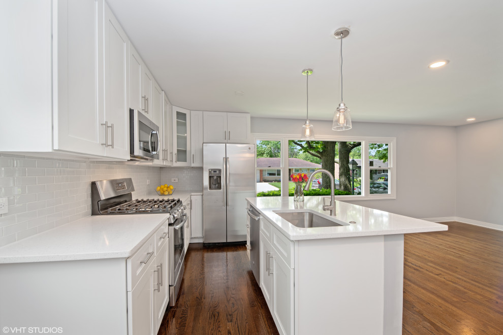 Example of a minimalist galley medium tone wood floor and brown floor eat-in kitchen design in Chicago with a single-bowl sink, shaker cabinets, white cabinets, quartzite countertops, white backsplash, glass tile backsplash, stainless steel appliances, an island and white countertops