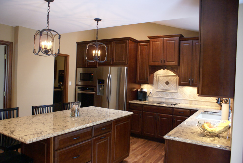 This is an example of a classic kitchen in Chicago with a submerged sink, raised-panel cabinets, dark wood cabinets, granite worktops, beige splashback, stone tiled splashback, stainless steel appliances, medium hardwood flooring and an island.