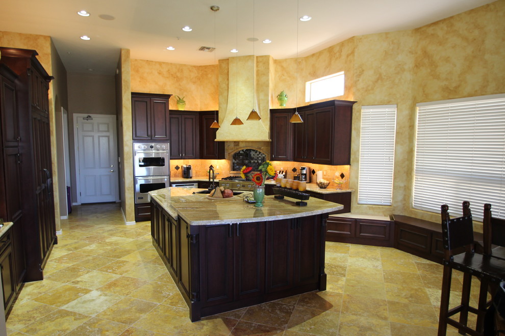 Example of a large transitional l-shaped travertine floor eat-in kitchen design in Phoenix with a double-bowl sink, raised-panel cabinets, dark wood cabinets, granite countertops, yellow backsplash, stone tile backsplash, stainless steel appliances and an island