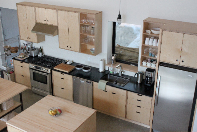 This is an example of a large industrial single-wall open plan kitchen in Vancouver with a submerged sink, flat-panel cabinets, light wood cabinets, composite countertops, stainless steel appliances, concrete flooring and multiple islands.