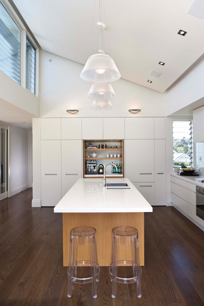 Inredning av ett modernt mellanstort kök, med en undermonterad diskho, vita skåp, bänkskiva i kvarts, vitt stänkskydd, glaspanel som stänkskydd, integrerade vitvaror, mellanmörkt trägolv, en köksö och brunt golv