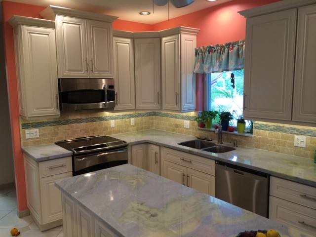 Photo of a medium sized traditional l-shaped enclosed kitchen in Miami with a double-bowl sink, raised-panel cabinets, white cabinets, granite worktops, multi-coloured splashback, ceramic splashback, stainless steel appliances, travertine flooring and an island.