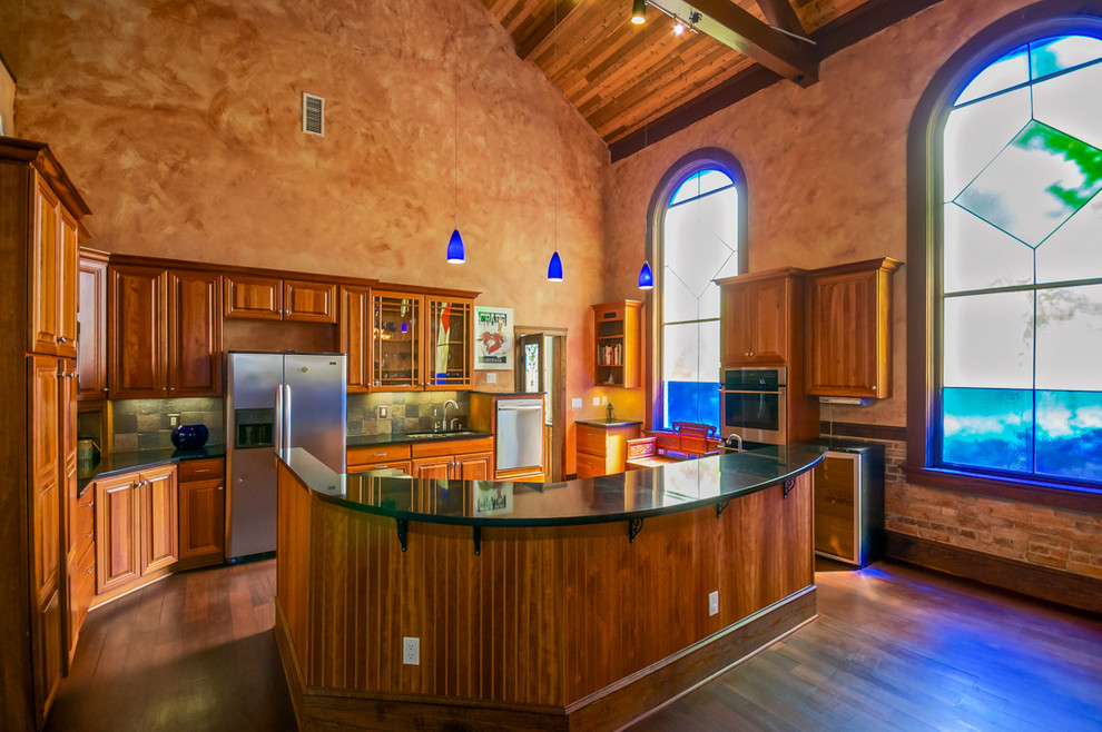 Large eclectic l-shaped open plan kitchen in Jacksonville with raised-panel cabinets, medium wood cabinets, green splashback, stone tiled splashback, stainless steel appliances, dark hardwood flooring and an island.
