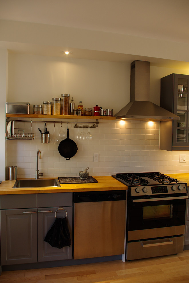 Exempel på ett litet eklektiskt linjärt kök och matrum, med en enkel diskho, luckor med glaspanel, grå skåp, träbänkskiva, vitt stänkskydd, rostfria vitvaror och ljust trägolv