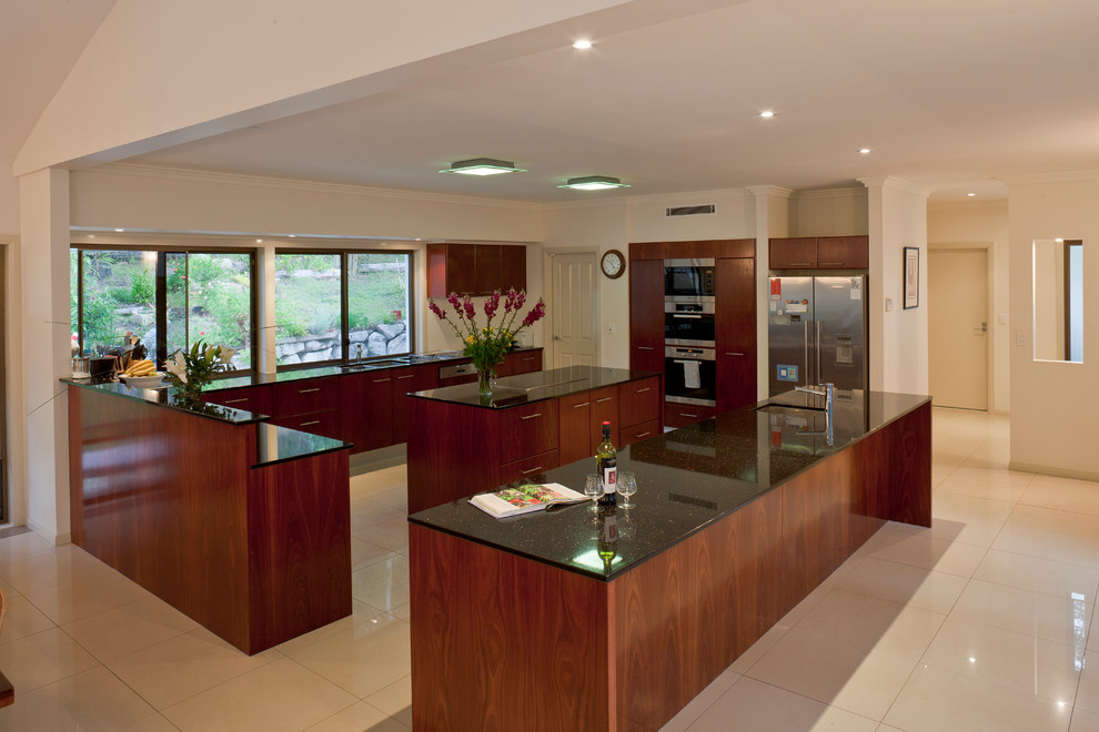 Expansive classic u-shaped enclosed kitchen in Brisbane with a double-bowl sink, shaker cabinets, dark wood cabinets, granite worktops, stainless steel appliances, porcelain flooring and multiple islands.