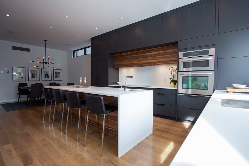 Design ideas for a medium sized modern galley kitchen/diner in Toronto with flat-panel cabinets, black cabinets, quartz worktops, white splashback, medium hardwood flooring and an island.