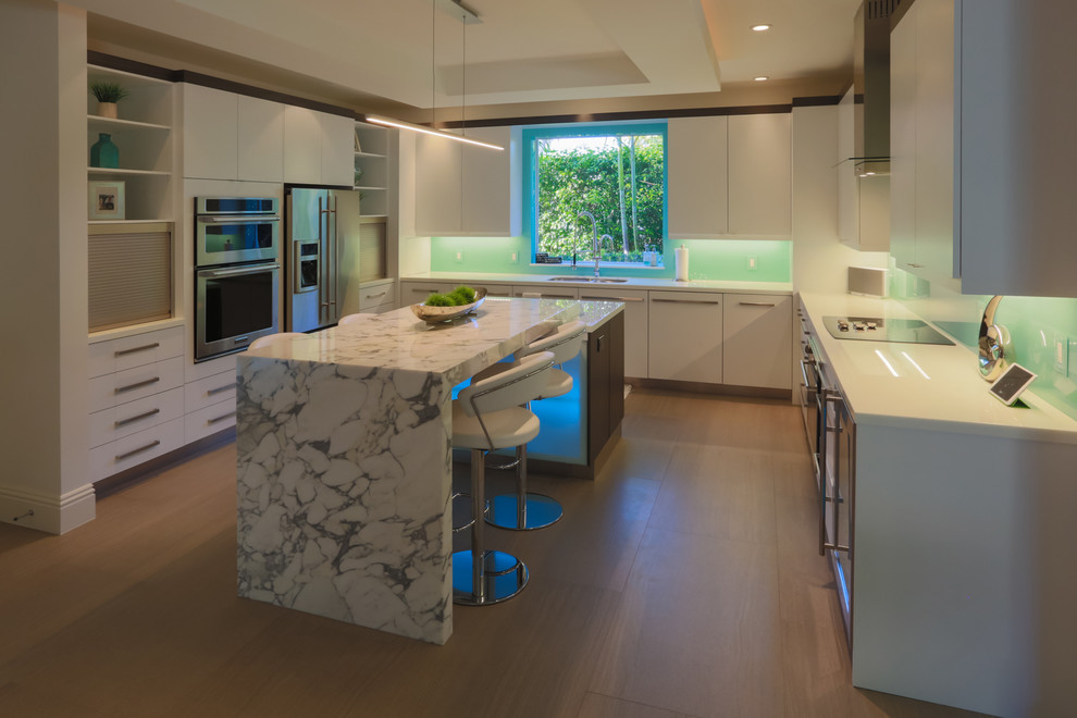 Foto på ett stort funkis kök, med en undermonterad diskho, släta luckor, vita skåp, marmorbänkskiva, blått stänkskydd, glaspanel som stänkskydd, rostfria vitvaror, klinkergolv i porslin och en köksö