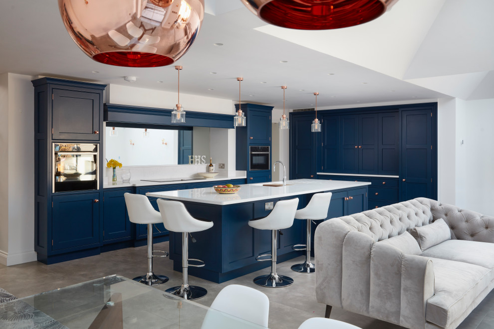 Cette image montre une grande cuisine encastrable design en L avec un évier encastré, un placard à porte shaker, des portes de placard bleues, une crédence miroir, îlot, un sol gris et un plan de travail blanc.