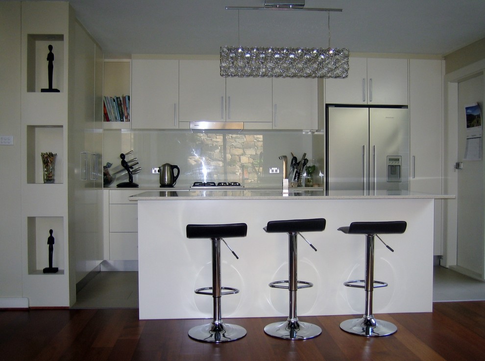 Modern inredning av ett mellanstort kök, med en undermonterad diskho, släta luckor, vita skåp, bänkskiva i kvarts, glaspanel som stänkskydd, rostfria vitvaror, klinkergolv i keramik och en köksö