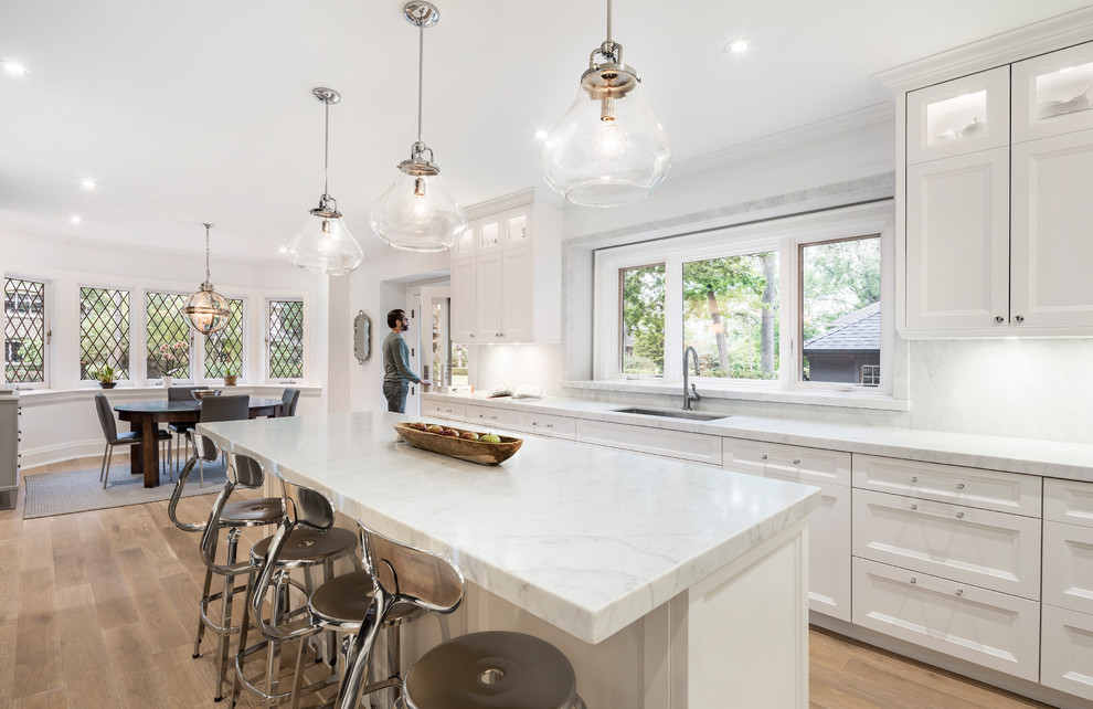 Eat-in kitchen - large transitional light wood floor and beige floor eat-in kitchen idea in Toronto with an undermount sink, white cabinets, marble countertops, white backsplash, marble backsplash, an island and recessed-panel cabinets