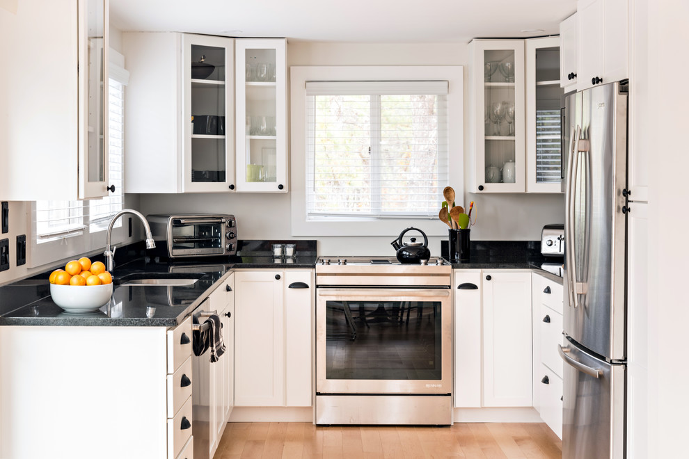 Klassische Küche ohne Insel in U-Form mit Unterbauwaschbecken, Glasfronten, Küchengeräten aus Edelstahl, hellem Holzboden und schwarzer Arbeitsplatte in Boston