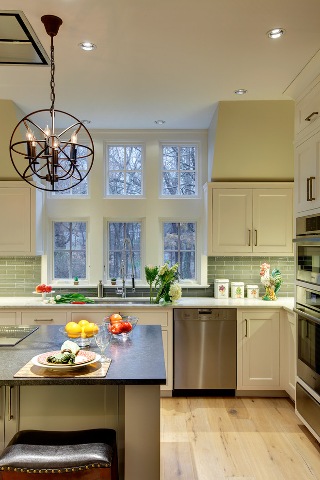 Large transitional u-shaped light wood floor enclosed kitchen photo in New York with a double-bowl sink, shaker cabinets, white cabinets, solid surface countertops, green backsplash, ceramic backsplash, stainless steel appliances and an island