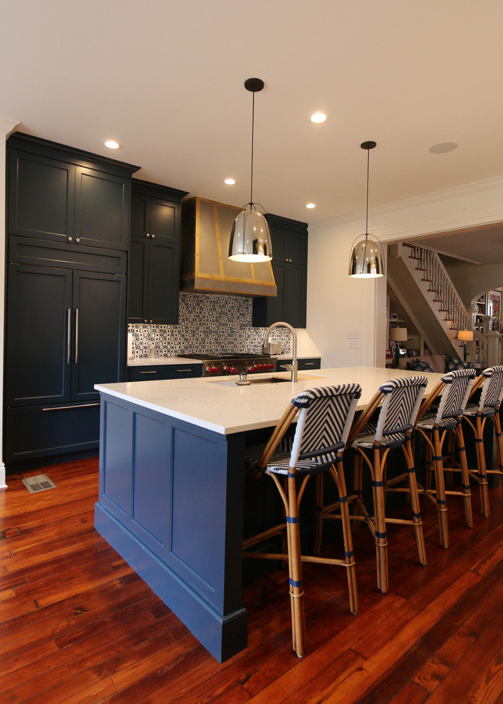 Inspiration for a mid-sized transitional medium tone wood floor and brown floor kitchen remodel in New Orleans with recessed-panel cabinets, blue cabinets, multicolored backsplash, ceramic backsplash, paneled appliances, an island and white countertops