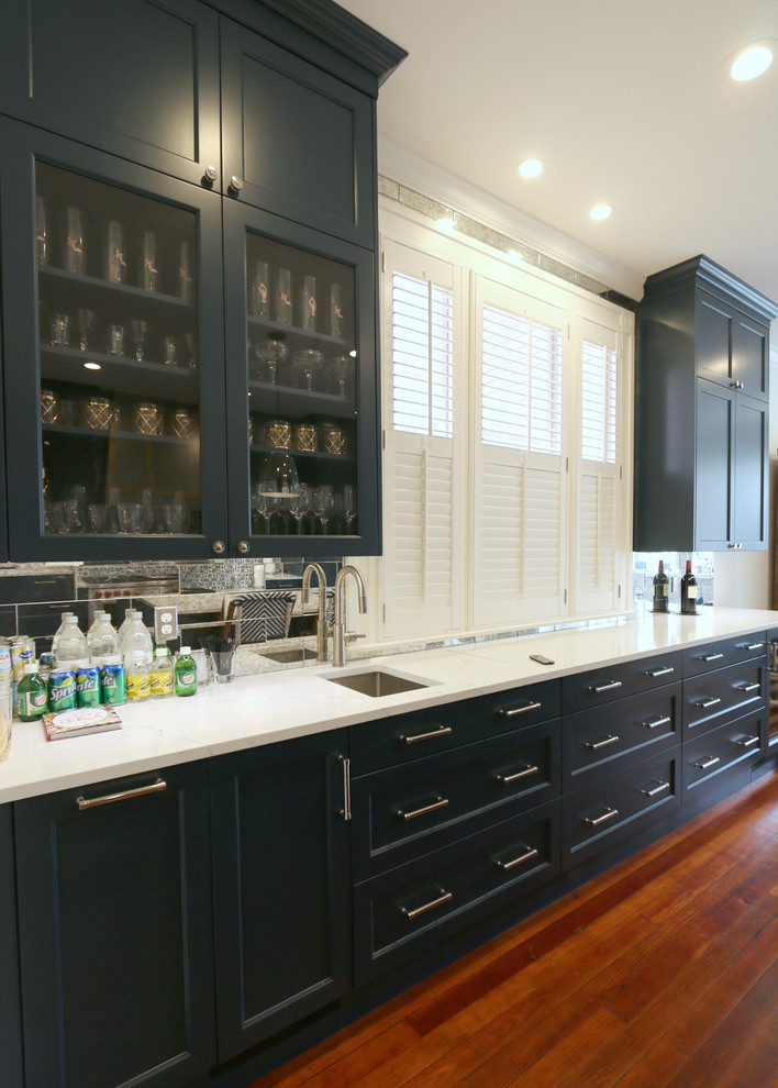 Immagine di un cucina con isola centrale chic di medie dimensioni con lavello sottopiano, ante con riquadro incassato, ante blu, paraspruzzi a specchio, pavimento in legno massello medio, pavimento marrone e top bianco