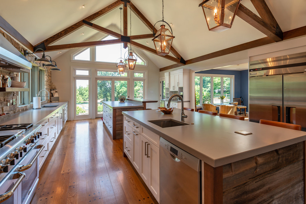 Example of a mid-sized country galley light wood floor and brown floor open concept kitchen design in Philadelphia with a drop-in sink, shaker cabinets, white cabinets, quartzite countertops, gray backsplash, stone tile backsplash, stainless steel appliances, two islands and gray countertops
