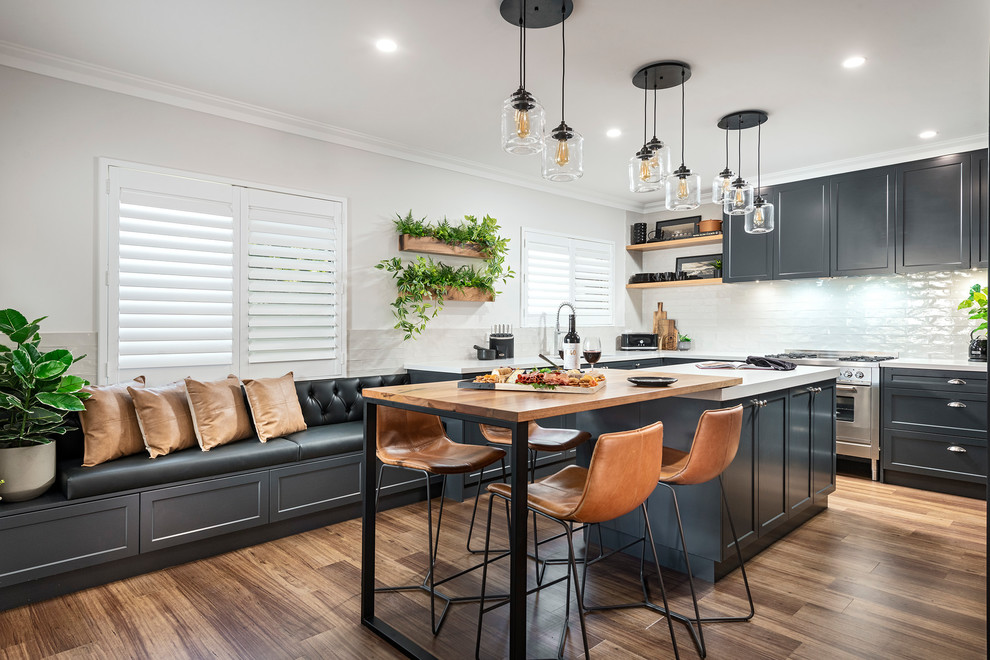 Idées déco pour une cuisine américaine classique avec un placard à porte shaker, des portes de placard noires, une crédence blanche, un électroménager en acier inoxydable, un sol en bois brun, îlot, un sol marron et un plan de travail blanc.