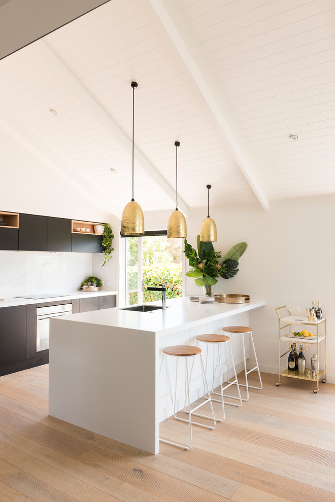 Zweizeilige Moderne Küche mit Unterbauwaschbecken, flächenbündigen Schrankfronten, schwarzen Schränken, Küchenrückwand in Weiß, hellem Holzboden, Halbinsel, beigem Boden und weißer Arbeitsplatte in Auckland