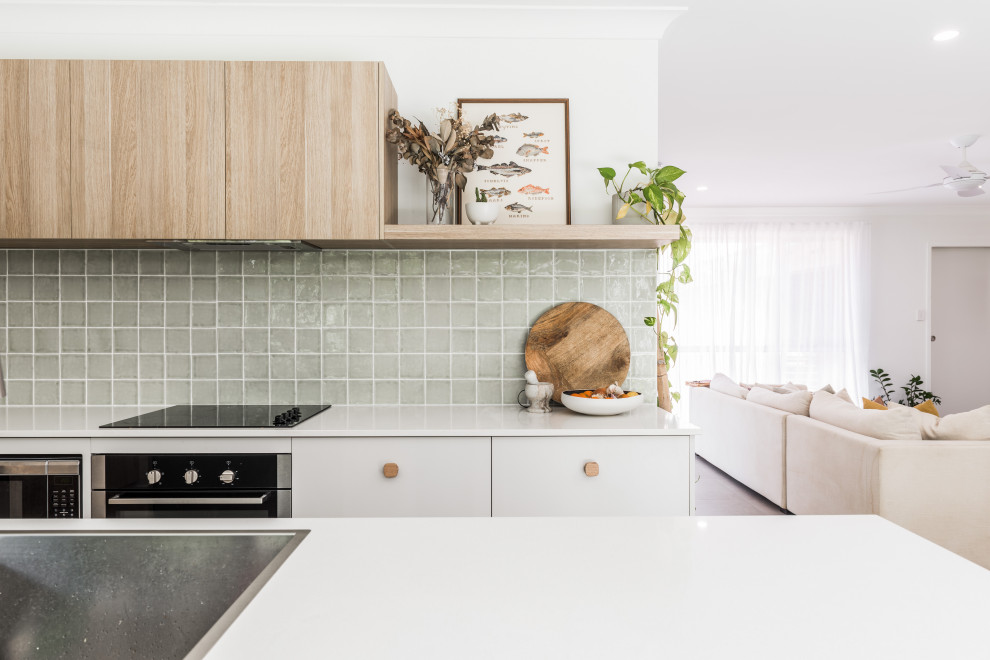 Modern inredning av ett kök, med skåp i ljust trä, grönt stänkskydd, stänkskydd i keramik, rostfria vitvaror och en köksö