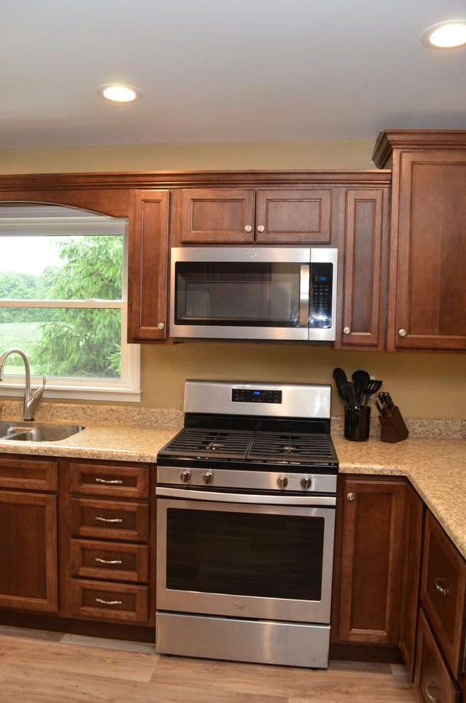 This is an example of a large traditional u-shaped kitchen/diner in Other with a submerged sink, recessed-panel cabinets, dark wood cabinets, laminate countertops, a breakfast bar, beige worktops, stainless steel appliances, light hardwood flooring and brown floors.