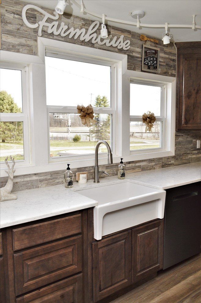 Foto på ett stort lantligt vit kök, med en rustik diskho, luckor med upphöjd panel, bruna skåp, bänkskiva i kvartsit, brunt stänkskydd, rostfria vitvaror, en köksö och brunt golv
