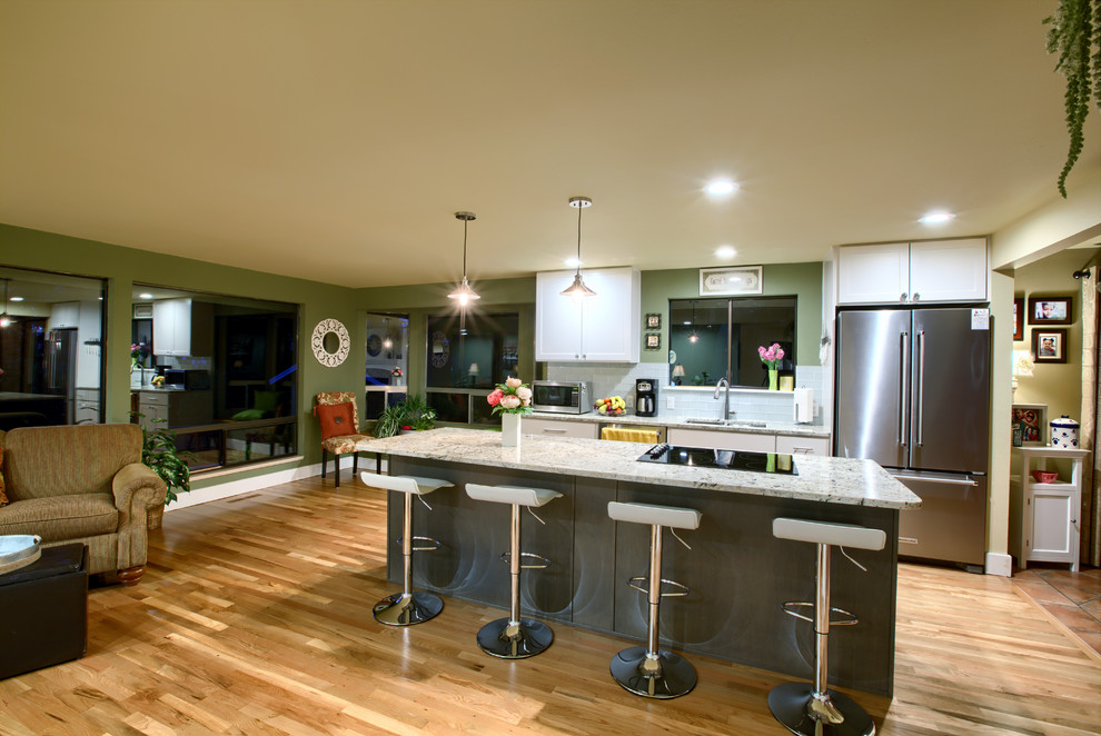 Exempel på ett mellanstort klassiskt linjärt kök med öppen planlösning, med skåp i shakerstil, vita skåp, granitbänkskiva, vitt stänkskydd, stänkskydd i tunnelbanekakel, rostfria vitvaror, ljust trägolv, en köksö och beiget golv