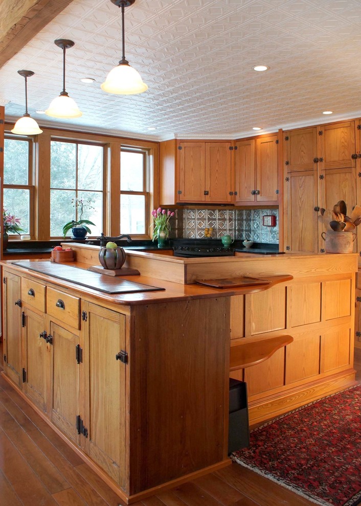 Amerikansk inredning av ett mellanstort kök, med en undermonterad diskho, luckor med infälld panel, skåp i mellenmörkt trä, bänkskiva i täljsten, stänkskydd med metallisk yta, stänkskydd i metallkakel, svarta vitvaror, mellanmörkt trägolv och en köksö