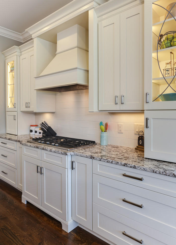Foto på ett mellanstort vintage kök, med en undermonterad diskho, luckor med infälld panel, vita skåp, granitbänkskiva, vitt stänkskydd, stänkskydd i keramik, rostfria vitvaror, mellanmörkt trägolv och en köksö