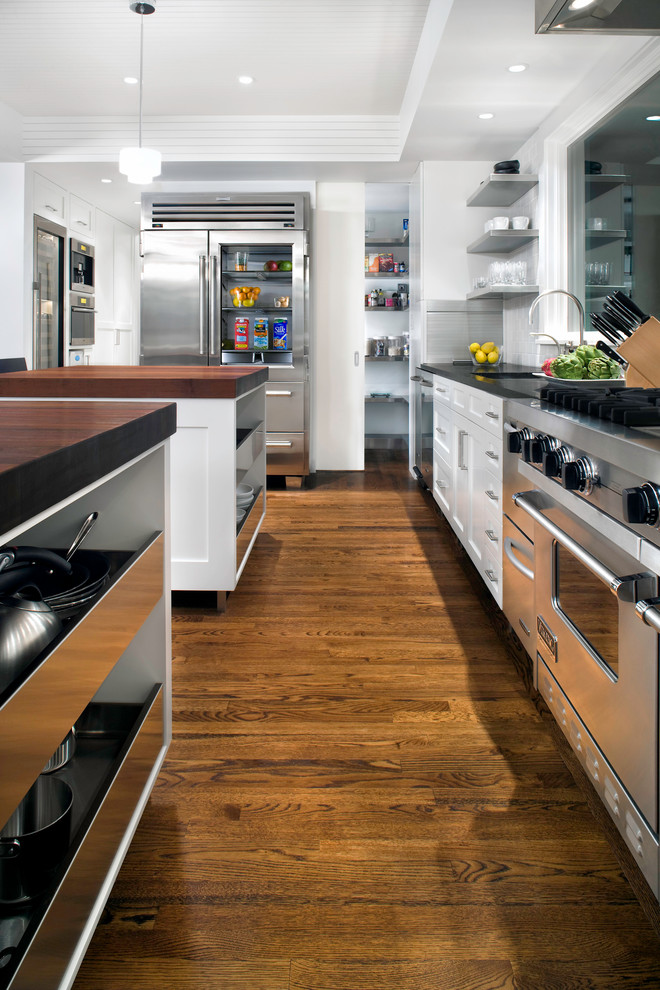Exempel på ett modernt kök med öppen planlösning, med en undermonterad diskho, luckor med infälld panel, vita skåp, träbänkskiva, vitt stänkskydd, stänkskydd i tunnelbanekakel, rostfria vitvaror, mörkt trägolv och flera köksöar