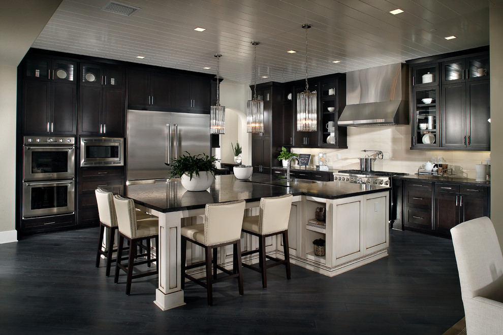 Example of a l-shaped dark wood floor eat-in kitchen design in San Diego with a farmhouse sink, shaker cabinets, black cabinets, granite countertops, beige backsplash, stone tile backsplash, stainless steel appliances and a peninsula