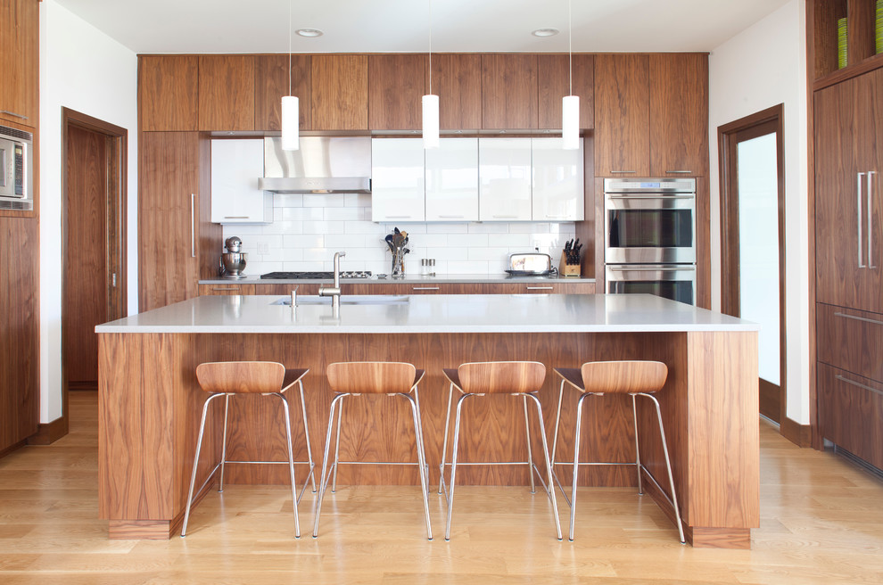 Offene Moderne Küche in U-Form mit flächenbündigen Schrankfronten, dunklen Holzschränken, Küchenrückwand in Weiß, Rückwand aus Metrofliesen und braunem Holzboden in Denver