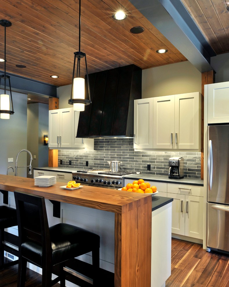 シアトルにあるトランジショナルスタイルのおしゃれなキッチン (落し込みパネル扉のキャビネット、御影石カウンター、黒いキッチンパネル、シルバーの調理設備) の写真
