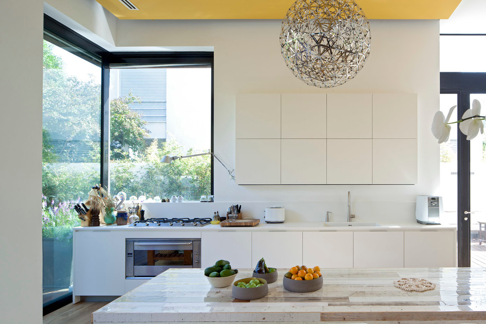 Moderne Küche mit flächenbündigen Schrankfronten, weißen Schränken, Küchenrückwand in Weiß und Küchengeräten aus Edelstahl in Tel Aviv