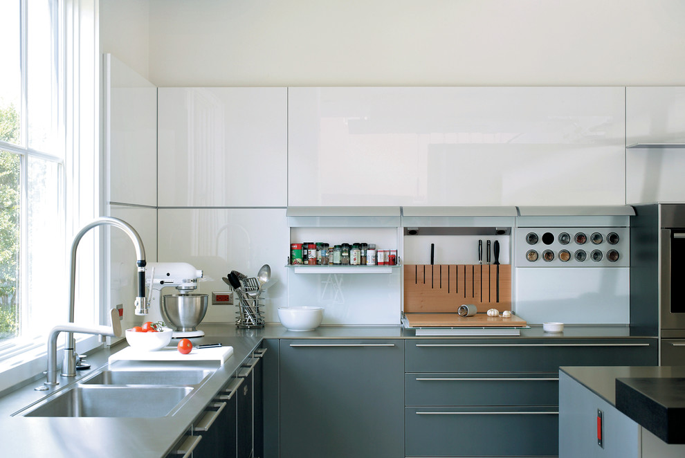 This is an example of a large contemporary grey and white u-shaped kitchen/diner in Little Rock with a double-bowl sink, stainless steel worktops, white splashback, an island, flat-panel cabinets, glass sheet splashback, stainless steel appliances, porcelain flooring and grey cabinets.