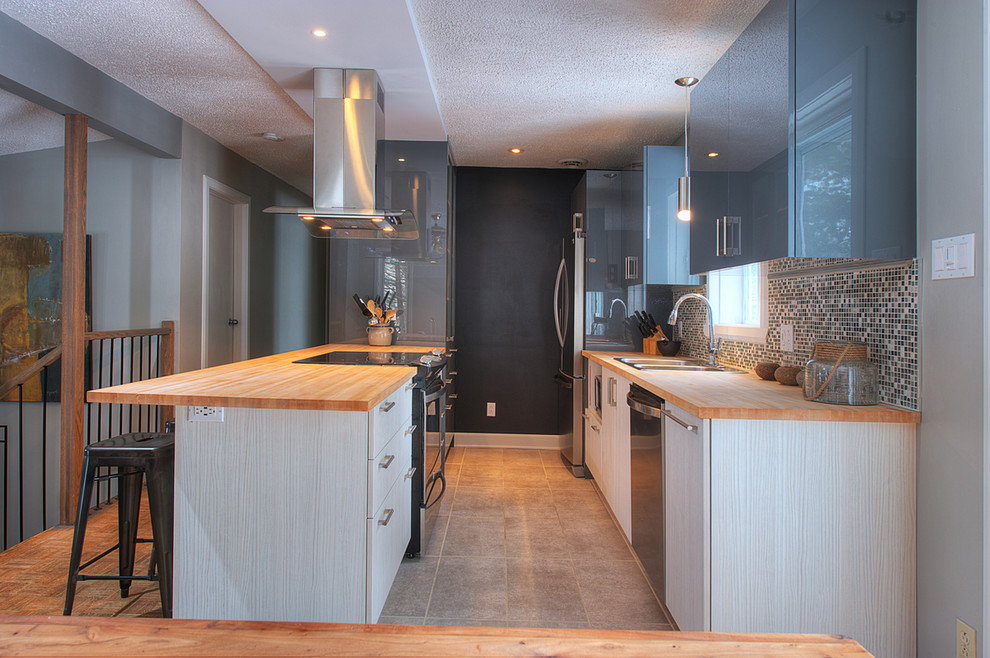 Small contemporary galley kitchen/diner in Montreal with a built-in sink, flat-panel cabinets, grey cabinets, wood worktops, beige splashback, mosaic tiled splashback, stainless steel appliances and porcelain flooring.
