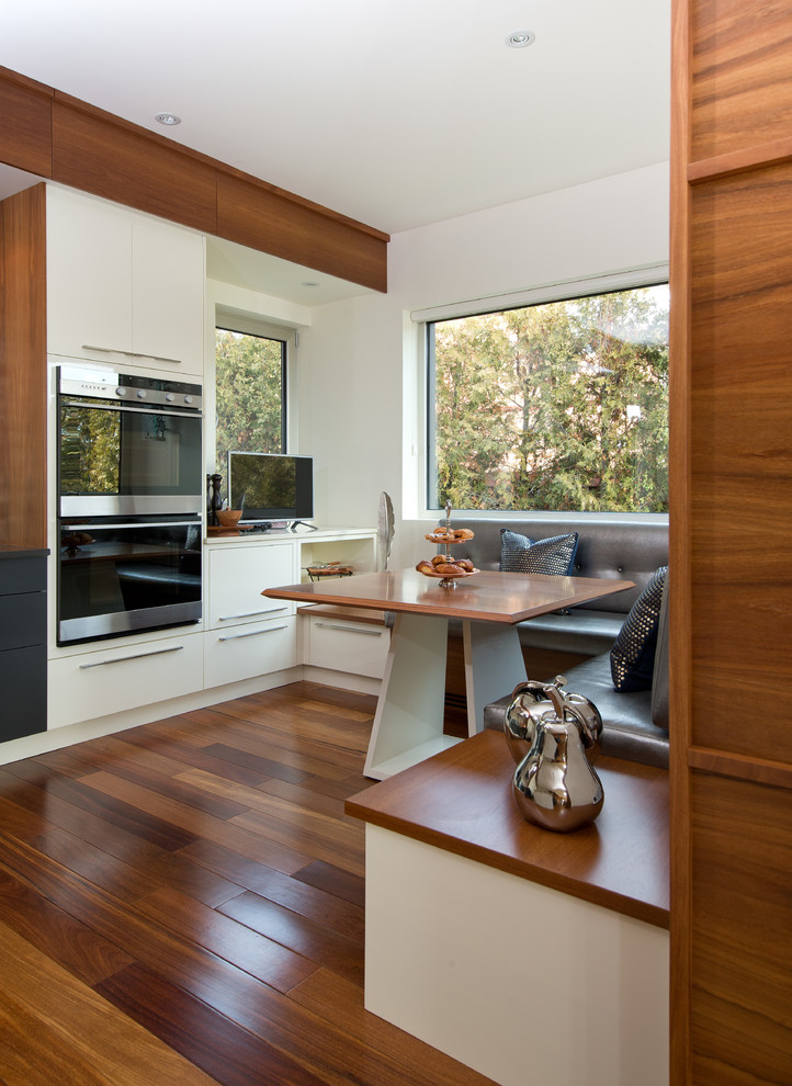 Foto di una cucina abitabile design con ante bianche, top in legno, elettrodomestici in acciaio inossidabile, pavimento in legno massello medio e nessuna isola