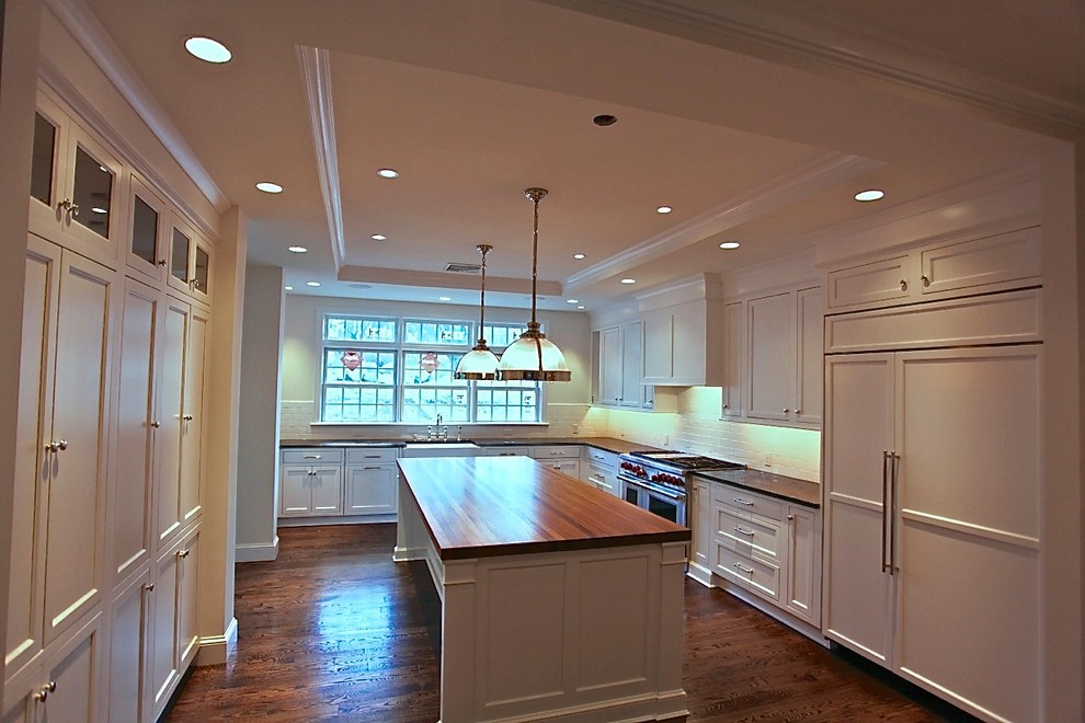 Exempel på ett avskilt, stort klassiskt kök, med en rustik diskho, luckor med infälld panel, vita skåp, träbänkskiva, vitt stänkskydd, stänkskydd i tunnelbanekakel, integrerade vitvaror, mörkt trägolv och en köksö